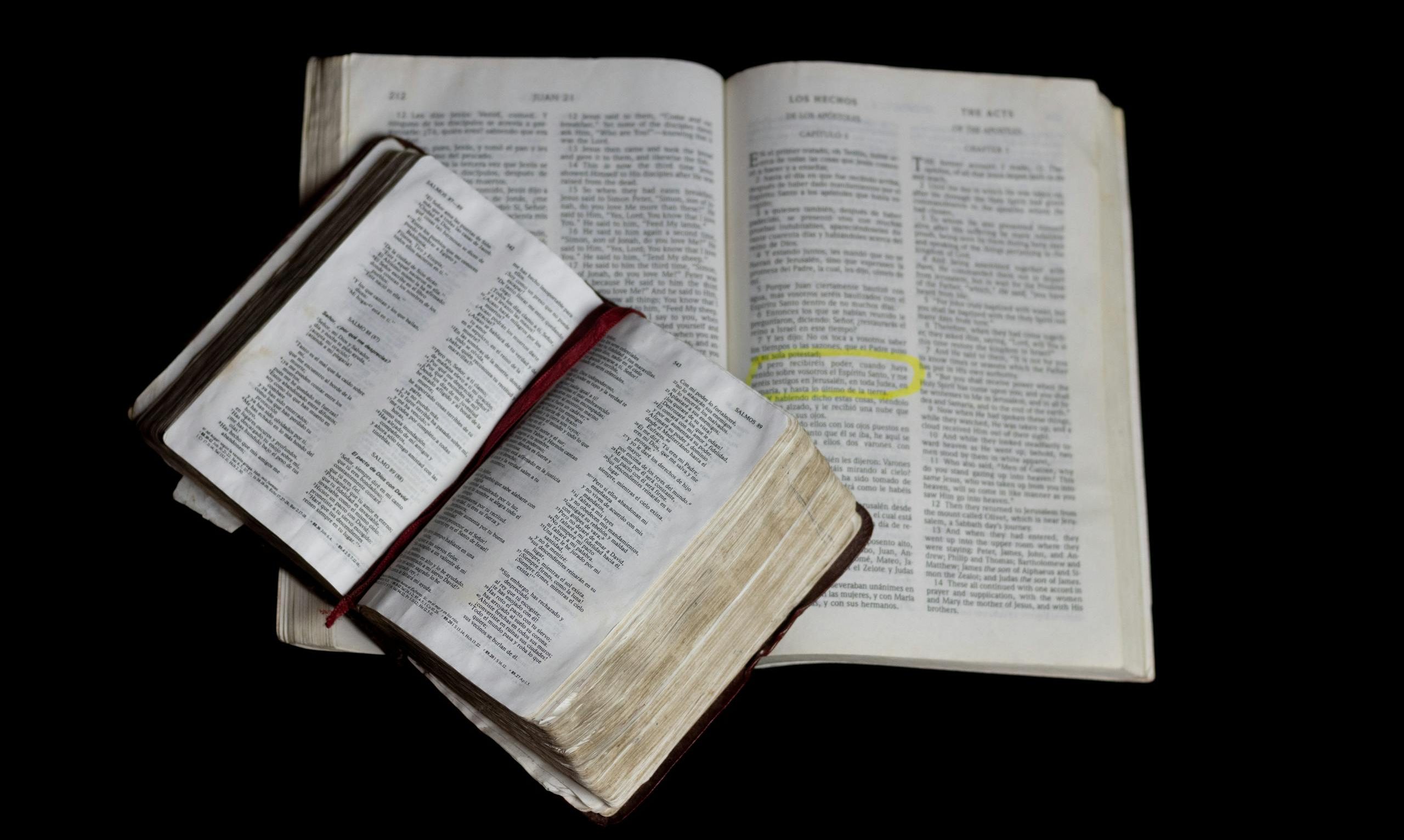 An open Bible on top of another against a plain black background.
